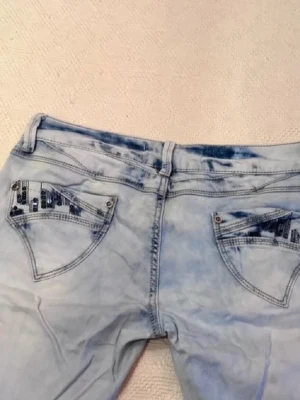 Bootcut ljusblå jeans med paljettdetaljer - Snygga bootcut jeans i ljusblå tvätt med slitningar och paljettdetaljer på bakfickorna. Jeansen har klassisk femficksdesign och är tillverkade i jeansmaterial. Säljer dessa jättesnygga jeansen då jag inte använder dem längre. Har använt ett antal gånger men har inga synliga slitningar. Skriv för måtten eller andra frågor. Annars tryck på köp nu🥰