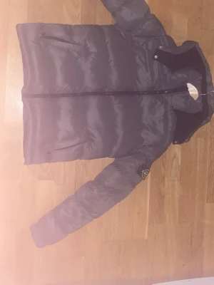  pufferjacka från Stone Island - Säljer en grå pufferjacka från Stone Island med ikonisk patch på ärmen. Jackan har huva, dragkedja framtill och två sidofickor med dragkedja. Materialet är glansig polyester och jackan är perfekt för kalla dagar. Stilsäker och clean look.