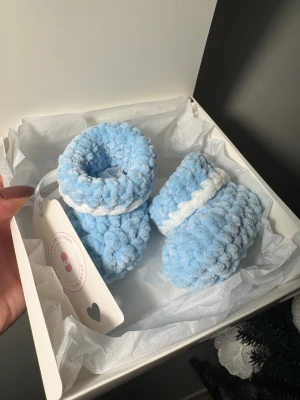 Virkade baby tofflor - Supersöta handgjorda baby tofflor i ljusblått och vitt, virkade i ett super mjukt garn. Skorna har en rund form och är riktigt gosiga för de minsta. Virkade av mig.   Storlek 0-3 månader.   Garnet är certifierat med OEKO-TEX® standard 100 produktklass 1. Produktklass 1 är högsta klass och gäller t ex textilier och leksaker tillverkade för spädbarn och småbarn.