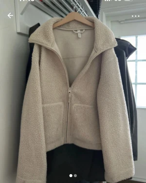 Beige teddyjacka med dragkedja - Mysig teddyjacka från H&M i beige färg med hög krage och två stora fickor framtill. Jackan har en rak passform och stängs med dragkedja. Perfekt för att hålla sig varm och se chill ut under höst och vinter.