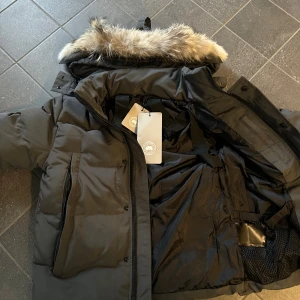 Grå jacka  -  Jackan har quiltad design, dragkedja och knappar framtill samt praktiska fickor. Perfekt för kalla vinterdagar och har en klassisk patch på ärmen.