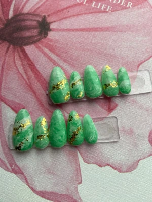 Gröna marmorerade lösnaglar med guld - Snygga lösnaglar i mandelform med marmorerat mönster i grönt och vitt, dekorerade med skimrande guldfolie. Naglarna har en glansig finish och passar perfekt för dig som vill sticka ut med en unik och trendig look.