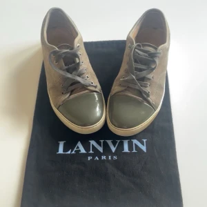 Lanvin sneakers med grön tå - Säljer ett par snygga sneakers från Lanvin i beige mocka med grön/grått blankt material. Storlek UK 6 ( 41-42) Skorna har snörning och en vit sula. Obs: snörena är lite trasiga på två av snörena. ( medföljer bara påse till skorna ) skriv vid intresse!⭐️( priset är inte hugget i sten )
