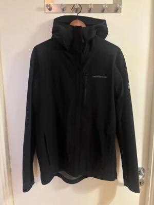 Svart vindjacka Peak Performance - Svart vindjacka från Peak Performance med huva och dragkedja framtill. Strl M. Pris kan diskuteras vid snabb affär, inga skambud. Inga byten.