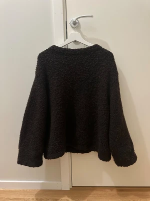 Mörkbrun fluffig tröja från NA-KD - Supermysig mörkbrun tröja från NA-KD i storlek S. Den har en fluffig, teddy-liknande yta och långärmade, lite loose passform. Perfekt för kalla dagar när du vill vara extra comfy. Rund hals och enkel design som är lätt att matcha med jeans eller leggings.