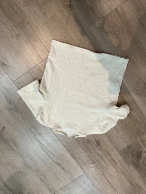 Vit/Biege ribbad polotopp från Zara - Säljer en vit/beige polotopp från Zara i storlek S. Toppen har en ribbad struktur och är tillverkad i ett mjukt material som känns skönt mot huden. Den har en enkel, stilren design med korta ärmar och passar perfekt till jeans eller kjol. Den är knappt använd.