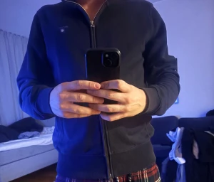 Marinblå zip-tröja från GANT - Snygg marinblå zip-tröja från GANT i storlek M. Tröjan har hel dragkedja framtill, ribbade muddar och två fickor. GANT-logga på bröstet och krage med diskret röd och vit rand på insidan. 