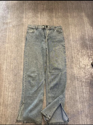 Wide jeans med slits nertill - Säljer ett par jeans med bred passform och slitsar nertill på benen. Jeansen är högmidjad och stängs med dragkedja och knapp.              OBS! Passar även storlek M