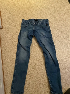 Replay Anbass blå jeans skinny fit - Snygga Replay Anbass jeans i blå tvätt med skinny passform. Klassisk femficksdesign, med Replay-logga på bakfickan och coola slitningar. Jeansen har normal midja och är gjorda i stretchigt denim för skön känsla. Perfekt för dig som gillar smalare jeans med stil.