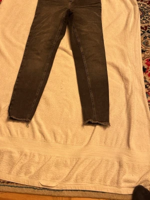 Mörkgrå skinny jeans med rå kant - Säljer ett par mörkgrå jeans med skinny fit och rå, fransad kant vid bensluten. Snyggt slitna detaljer och smal passform som sitter tajt längs benen. Perfekta för dig som gillar en modern och edgy look.