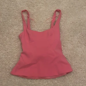 Rosa topp från Zara med rosett - Supersöt rosa linnetopp med breda axelband och en stor rosett i ryggen. Toppen har en figurnära passform och är tillverkad i ett slätt syntetmaterial som ger en snygg siluett. Köptes i våras men knappt använd pga att den var lite för stor. 