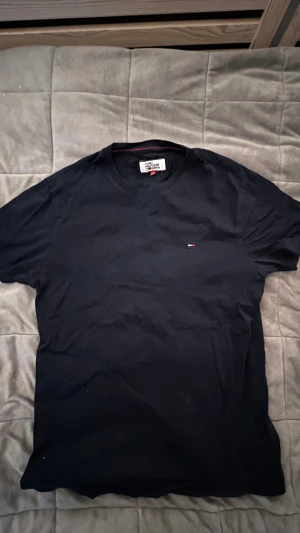 Mörk blå t-shirt från Tommy Hilfiger - Snygg mörk blå t-shirt från Tommy Hilfiger Denim med klassisk rund hals och liten broderad logga på bröstet. T-shirten är i mjuk bomull och har en enkel, stilren look som passar perfekt till jeans eller shorts.