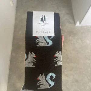 Svarta strumpor med ekorrmotiv Bengt & Lotta - Svarta strumpor från Bengt & Lotta med gulligt ekorrmotiv i ljusgrått och ljusblått, samt små röda detaljer. Tillverkade i mjuk merinoull som håller fötterna varma och sköna. Perfekt för dig som vill ha något unikt och snyggt på fötterna.