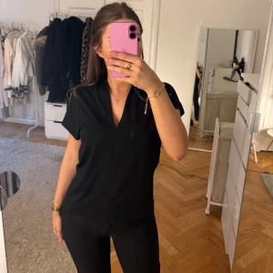 Svart v-ringad blus med kort ärm - En svart blus med v-ringning och korta ärmar. Modellen är lite lösare och har en snygg vikt krage upptill. Perfekt till jeans eller kostymbyxor för en clean look.