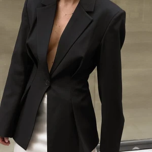 Svart figursydd blazer från NA-KD - NA-KDs bästsäljare. En svart figursydd blazer från NA-KD. Passformen är tight på kroppen och passar så fint till utekvällen. Helt ny med lapp kvar! 