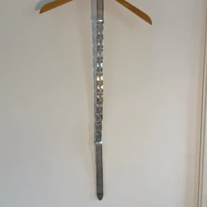 Silvrigt med metallplattor - Trendigt smalt bälte i silverfärgad metall med rektangulära metallplattor längs hela bandet. Bältet har ett coolt, futuristiskt uttryck och ett klassiskt spänne i metall. Perfekt för att ge din outfit en edgy touch. 