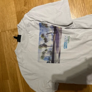 Vit COOLMAX t-shirt med tryck - Vit t-shirt från COOLMAX med färgglatt tryck av en basketplan och palmer på bröstet. Klassisk rund hals och korta ärmar. Materialet är lätt och andas, perfekt för varma dagar. COOLMAX EcoMade-logga tryckt under motivet.