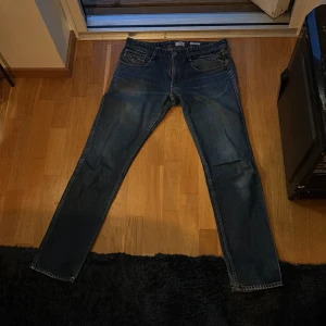 Replay Anbass jeans blå 33/34 - Säljer ett par Replay Anbass jeans i klassisk blå tvätt med snygga slitningar. Jeansen har fem fickor, rakt snitt och röda sömmar på insidan av linningen. Tillverkade i bomull och passar dig som gillar en modern och stilren look. Vid frågor och funderingar kan ni skriva, pris kan diskuteras