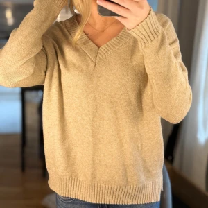 Beige stickad tröja från Vila - Mysig beige stickad tröja från Vila med v-ringad hals och ribbade muddar. Perfekt för lager-på-lager och passar till jeans eller kjol. Långärmad och i en klassisk, avslappnad passform.