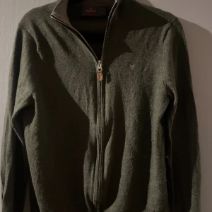 Olivgrön zip från Morris  - Det är en fin full zip från märket Morris i merinoull i mörk olivgrön. Varm och skön i vinter. Den står strl S men jag skulle säga den är liten i storlek och passar mig perfekt som är 160 cm lång. Se bilder.