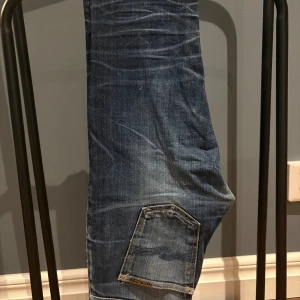 Nudie Jeans blå denimjeans 29/32 - Säljer ett par klassiska nudie selvage jeans med snygga slitningar och fin kontrast. Jeansen är i modellen grim tim vilket är en slim straight passform. Det ända problemet med jeansen är knappen högst upp vid gylfen har ramlat av men om man går till en nudie butik repareras det gratis. Nypriset är över 2000 