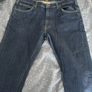 Lee Daren Zip Fly jeans mörkblå W36 L32 - Mörkblå jeans från Lee, modell Daren Zip Fly. Klassisk femficksdesign med Lee-logga på bakfickan och läderpatch i midjan. Jeansen har gul kontrastsöm och dragkedjegylf. Perfekt passform och tidlös look.