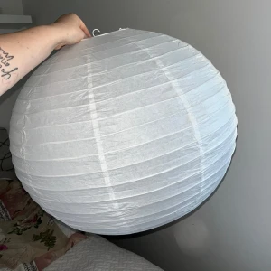 Rispapperslampa - Stor, rund rispapperslampa i vitt med metallstomme. Klassisk design. En liten reva och missfärgning som jag inte försökt att få bort syns vid öppningen, men i övrigt i gott skick. Perfekt för vardagsrum eller sovrum. Ca 70cm