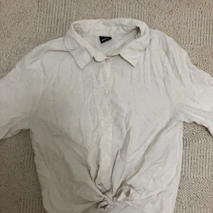 Vit skjorta med knyt från Gina Tricot - Snygg vit skjorta från Gina Tricot i storlek 36. Skjortan har klassisk krage, korta ärmar och knyt framtill för en chill vibe. Tillverkad i mjukt bomullstyg och har knappar längs hela framsidan. Perfekt för dig som gillar enkel och clean stil.