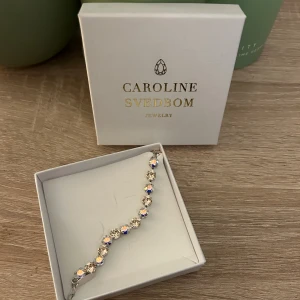 Glittrigt armband från Caroline Svedbom - Superfint armband från Caroline Svedbom med gnistrande, runda kristaller i silverfärg. Stenarna har en skimrande effekt som reflekterar olika färger beroende på ljuset. Helt nytt, aldrig använt då jag tyvärr bara använder guldsmycken! Nypris cirka 900-1000kr