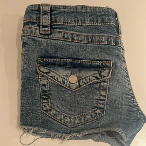 Blå jeansshorts med fransig kant - Låg midjade blå jeans shorts från Gina, med fina bakfickor.