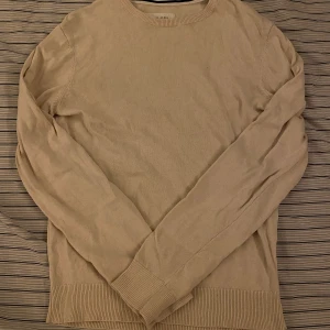 Beige stickad tröja från Pier One - Snygg beige stickad tröja från Pier One med rund hals och ribbade muddar vid ärmslut och nederkant. Perfekt för dig som gillar enkel och clean stil. Långärmad modell som passar till jeans eller chinos.