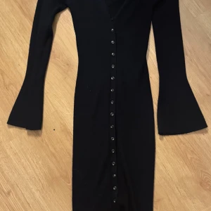 Svart långärmad klänning med utsvängda ärmar och knappar - Svart långklänning med lång ärm och utsvängda ärmslut. Lite tjockare och varmare material.