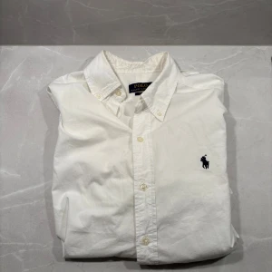 Ralph lauren skjorta - Klassisk vit skjorta från Polo Ralph Lauren med broderad logga på bröstet. Skjortan har knappar framtill och krage, perfekt för en clean och stilren look. Bara att höra av er vid frågor eller funderingar.