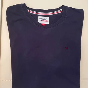 Mörkblå t-shirt från Tommy Jeans - Snygg mörkblå t-shirt från Tommy Jeans med klassisk rund hals och liten broderad logga på bröstet. Tillverkad i mjuk bomull och har korta ärmar. Perfekt för en clean och stilren look.