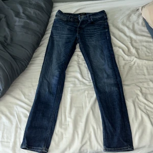 Blå tapered jeans Jack & Jones 28/32 - Säljer ett par blå jeans från Jack & Jones i modellen Tapered/Mike. Normal midja och avsmalnande ben. Materialet är jeans med snygga slitningar och kontrastsömmar. Jeansen är bara använda någon enstaka gång och har inga tecken på användning. Säljer pågrund av att dom är för små.