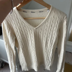Vit kabelstickad tröja från Stenströms - Snygg vit kabelstickad tröja från Stenströms med v-ringad hals och långa ärmar. Tröjan har klassiska stickade detaljer och ribbade muddar vid ärmslut och nederkant. Perfekt för dig som gillar stilrena och tidlösa plagg.