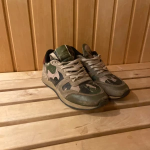 Valentino Rockrunner sneakers camouflage - Säljer ett par Valentino Rockrunner sneakers med ikoniskt camouflage-mönster i grönt, beige och svart. Skorna har detaljer i mocka, skinn och textil samt röda hälpartier och nitar på sulan. Klassisk snörning och platt sula. Perfekt för dig som vill sticka ut med lyxig streetstyle.