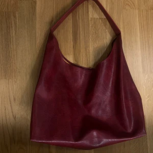 Röd axelväska i skinnimitation - Hel ny inte använd använd Stilren röd axelväska i skinnimitation med enkel design och generös storlek. Väskan har en bred axelrem och mjuk, slouchy form som gör den perfekt att bära över axeln. Perfekt för dig som gillar minimalistiska accessoarer med färg.