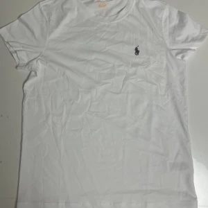 Vit t-shirt från Polo Ralph Lauren - Klassisk vit t-shirt från Polo Ralph Lauren med rund hals och korta ärmar. Liten broderad logga på bröstet. Tillverkad i mjuk bomull som känns skön mot huden. Perfekt basic-plagg att ha i garderoben.