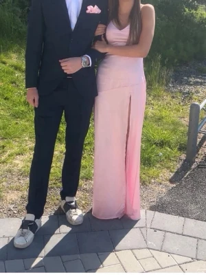 Ljusrosa balklänning satin - Säljer vidare en elegant ljusrosa långklänning med smala axelband och öppen rygg med snygg snörning. Klänningen har en slits framtill och figurnära passform som framhäver siluetten. Man kan knyta klänningen så den passar xs-s. Perfekt för student eller bal! Materialet känns mjukt och följsamt. Använd 1 gång 