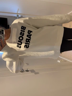 Vit sweatshirt Bisous Paris från H&M - Säljer denna trendiga vita sweatshirt med svart text 'BISOUS PARIS' på bröstet. Använd fåtal gånger då den är för stor