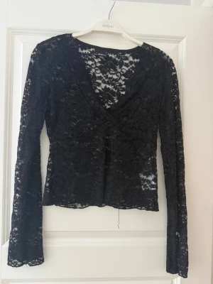 Svart spetsblus med v-ringning - Snygg svart blus i spets med v-ringad hals och långa ärmar från Gina