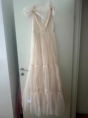 Balklänning i champange/ljusrosa - Supersöt balklänning i tyll som är oanvänd. Rosetter på axlarna men den går att ta av. Står att det är en xxs men skulle säga att den är en xs🩷 OBS! upptäckte ett hål nu i efterhand och vet inte hur det kan ha kommit då klänningen är oanvänd. Hålet är i tyllen så det syns inte när klänningen bärs, kommer inte heller synas om man syr upp klänningen. Men sänker priset. 
