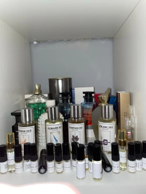 Byte - Samling av parfymer och doftprover från olika märken. Flera flaskor i glas med metallock, bland annat flaskor märkta Toliman 22.0, Alimarin 15.1, Thompson 41.0 och Leblanc 24.0. Färgerna varierar mellan transparent, grönt och blått. Inkluderar både större flaskor och små provrör.