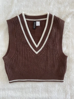 Brun stickad väst med v-ringning - Snygg brun stickad väst från H&M med v-ringad hals och vita ribbade detaljer vid halsringning och nederkant. Har inga defekter