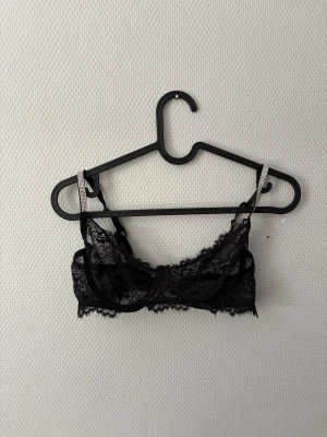 Svart spets-bh med strassdetaljer - Snygg svart bh i genomskinlig spets med dekorativa strassdetaljer på axelbanden. Bh:n har bygel och justerbara axelband samt hakknäppning bak. Perfekt för dig som gillar en feminin och trendig look. Inga defekter alls förutom att lappen är förstörd med storlek osv!💓🌸