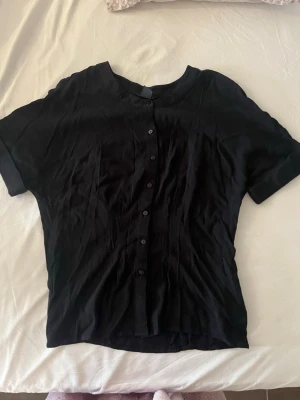 Svart kortärmad blus med knappar - Svart blus med korta ärmar och knäppning framtill.  Skulle säga den är lite tightare i midjan.
