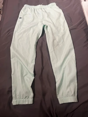 Ljusgröna mjukisbyxor från Lacoste - Säljer ett par ljusgröna mjukisbyxor från Lacoste med klassisk krokodillogga på vänster sida. Byxorna har resår i midjan och vid bensluten för en skön passform. Tillverkade i ett lätt och mjukt material som passar perfekt för chill dagar.