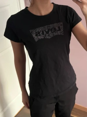 Svart Levi's t-shirt med logga - Snygg svart t-shirt från Levi's med klassisk logga i ett sprucket mönster på bröstet. T-shirten har rund halsringning och korta ärmar. 