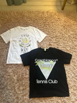 Casablanca t-shirts med tryck - Två t-shirts från Casablanca, en vit med färgglatt Casa Way-tryck och en svart med stort Casablanca Tennis Club-tryck framtill. Båda har rund hals och kort ärm, perfekt för en sportig och trendig look. Båda för 800. 